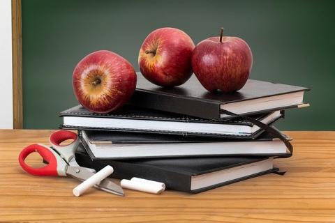 Stack of books and school supplies with 3 apples on top